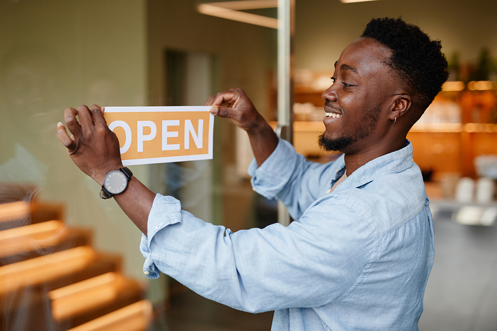 A man putting an OPEN sign on a business door